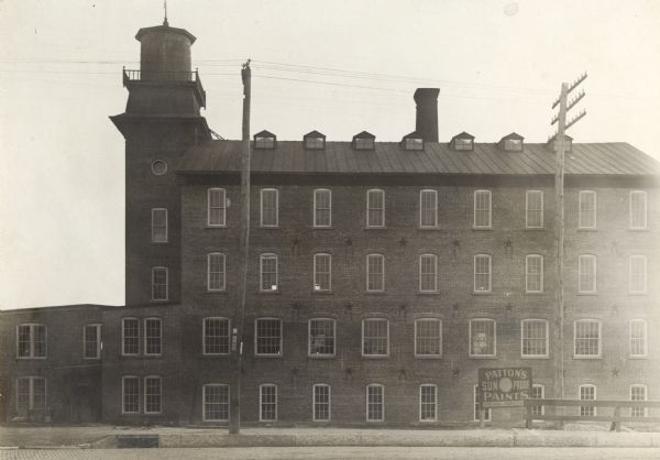 Exterior view of a woolen mill with an advertisement sign for Patton's Sun Proof-Paints in the front.