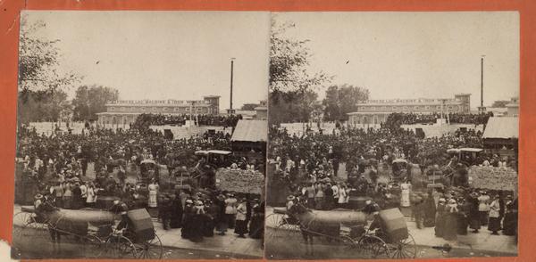 Stereograph view of a large crowd of people on a construction site. There is a horse and carriage with the Fond du Lac Machine & Iron Works in the background.
