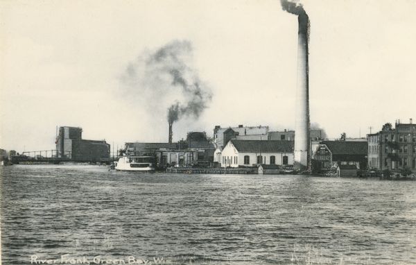 View from Fox River of chimneys, buildings, and boat. Caption reads: "River Front, Green Bay, Wis."