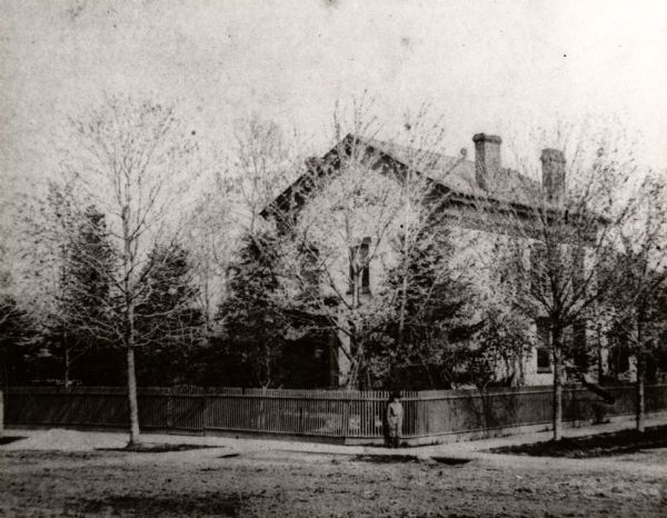 The home of I.G. Merrill on the corner of Ann Street (now called Sheridan Road) and Prairie Avenue. A person is standing in front of the fence at the corner.