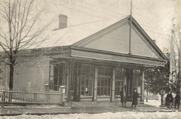 The First National Bank that was the Iowa County Building between 1843 and 1860, then the W.T. Henry Bank and post office. Men are standing outside on the sidewalk in front of the bank.