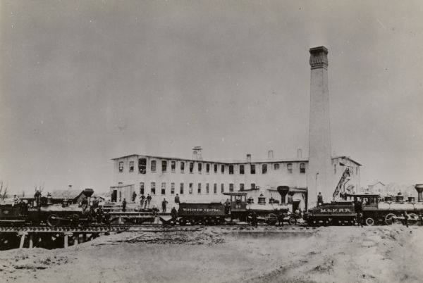 The George A. Whiting Paper Mills with men posing on switcher engines in front of the buildings. The engines are, (left to right): Chicago and Northwestern Railway No. 124, Wisconsin Central Railway No. 24 and Milwaukee and Northern Railroad No. 2.