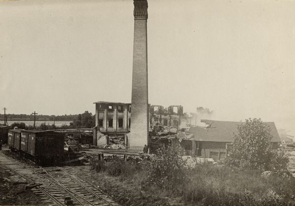 Slightly elevated view of the George A. Whiting Paper Mill after a fire on August 24, 1888. Sixteen men were killed by the explosion of a bleacher; the bleacher exploded as the night fire-man had no time to turn off the steam as he escaped the fire. The bleacher hit the office (the building to the right of the chimney) and landed on the rails where the sixteen men that were killed were standing.