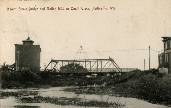 View from river toward the bridge and mill. Caption reads: "Hewitt Street Bridge and Roller Mill on Oneill Creek, Neillsville, Wis."