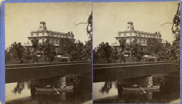 Stereograph of the Townsend House, a resort hotel. In the foreground there are three people in a rowboat, rowing under a bridge where four other people are standing.