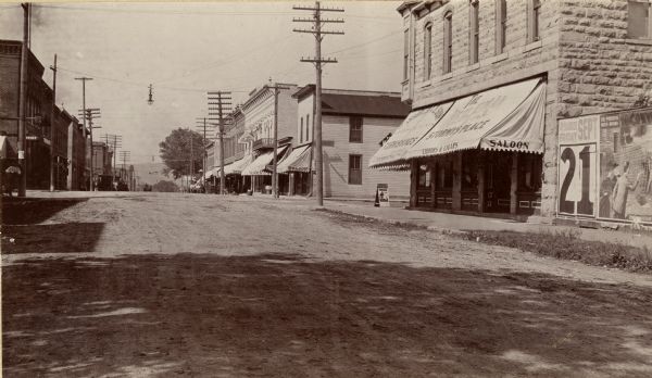 Bluff street looking west. Posters are on a wall on the far right next to a building with an awning that reads: "Saloon".
