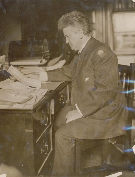 Senator Robert M. La Follette Sr., posed sitting at his desk reading a letter.