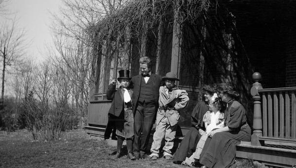 Robert M. La Follette, Sr., at Maple Bluff Farm with three of his children, Philip F. La Follette, Robert M. La Follette, Jr., and Mary, all of whom are dressed in costume.  Mrs. La Follette is seated on the porch steps (half hidden) and with her is Nellie Dunn, the secretary in La Follette's law office.