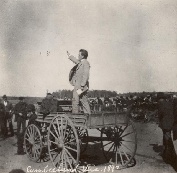 Robert M. La Follette, Sr., with his fist in the air, speaking from the back of a wagon. It was in part due to his vigorous speaking style that La Follette won the nickname "Fighting Bob." This image is one of a series of views of his appearance at a fair in Cumberland, Wisconsin, in 1897. After three unsuccessful campaigns during which he brought his reform message to Wisconsin at events such as this, La Follette was elected governor of Wisconsin in 1900.