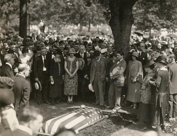 Funeral of Senator Robert M. La Follette, Sr., at Forest Hill Cemetery in Madison. Mourners gathered around La Follette's flag-draped coffin include Philip Fox La Follette, Belle Case La Follette, and Robert M. La Follette, Jr., (in front of the tree) and La Follette son-in-law George Middleton to the right of the tree.