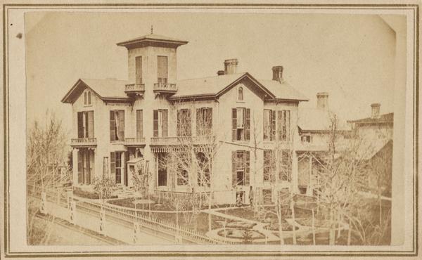 Elevated view of the Robert M. Bashford house on Pinckney and Gilman Streets. A man wearing a hat stands in the landscaped yard near a small child wearing a coat and hat.