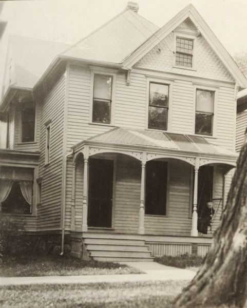 Exterior view of the Merrick residence, with a woman sitting on a swing on the front porch.