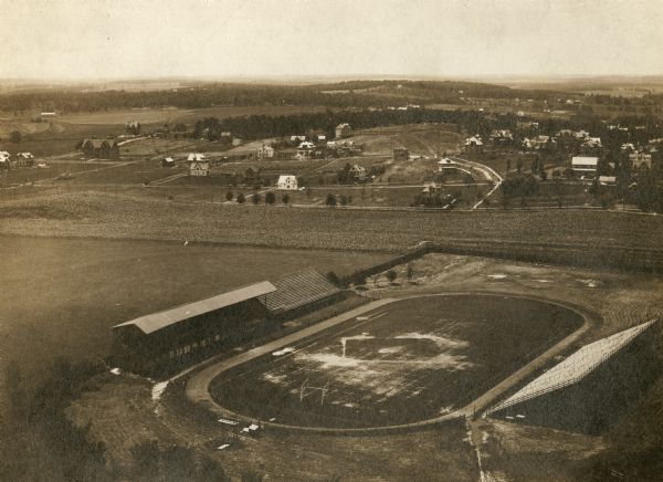 Aerial view looking north over Camp Randall stadium towards University Heights. In the right-center area of the photograph, the Wayland J. Chase residence, at 1727 Summit Avenue, is under construction. The Randall School, located at the intersection of Regent Street and Spooner Avenue is visible in the upper left.