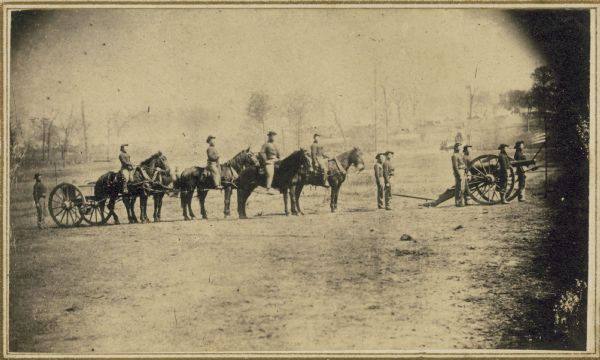 Soldiers of the 3rd Wisconsin Artillery at Camp Randall man a cannon on wheels, while other men on foot and on horseback follow.
