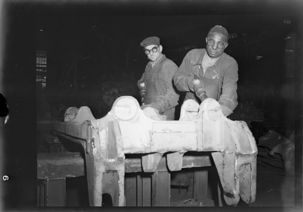Workers chipping imperfections from a rough casting.