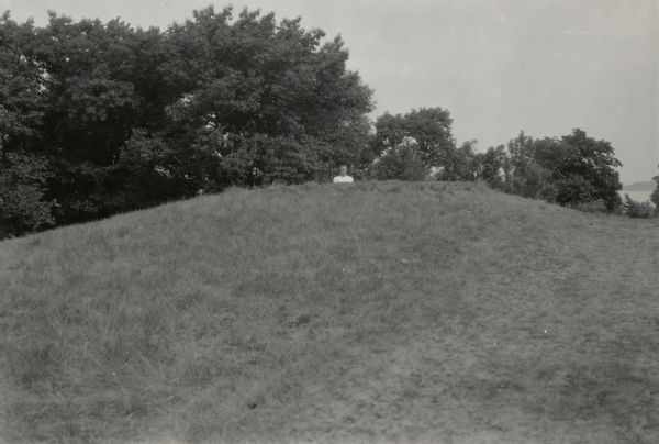 A man poses behind a large conical Native American burial mound near the center of Picnic Point on the University of Wisconsin-Madison campus.