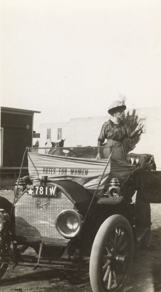 Suffragist Katherine Waugh McCullough speaking from an open car. A banner on the car reads: "Votes for Women."