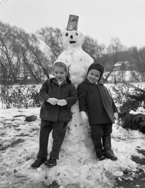 Winter scene with two children leaning against a snowman.