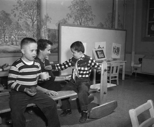Patricia Mathisen (Mrs. George), member of Kappa Kappa Gamma sorority alumnae group, sponsor of the Nursery School for Slow Learners at the First Congregational Church, is playing with two boys on a "rocking train."