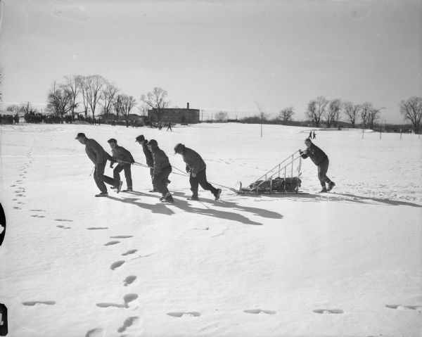 Boy scout sled team participating in the Klondike Derby sled race. The boys are pulling the sled on the Monona Golf Course, with Nichols School in the background. Nearly 300 scouts from the Dane County area participated in "Operation Klondike" which tested the boys in first aid, ice rescue, fire building and compass knowledge. 

