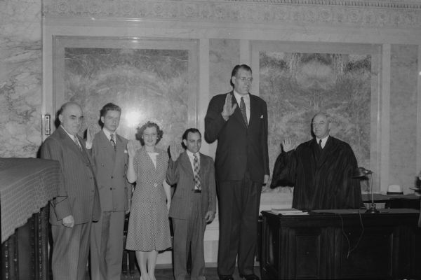 Clifford Thompson, the second tallest man in the world, being sworn into the Wisconsin state bar at the Wisconsin State Capitol by Justice Elmer E. Barlow. Others from left to right: Francis Sweitlik, dean of the Marquette Law School, Robert Schoen, Jane O'Meila, James D"Amato, and Clifford Thompson.  All were students at the Marquette Law School in Milwaukee.
