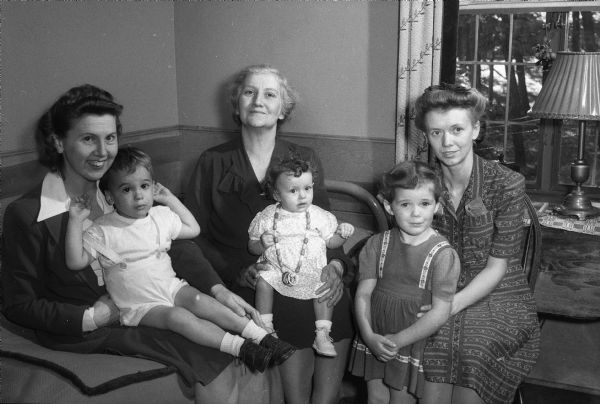 Three women and three children at a meeting of the Madison Home Economics Club with the theme "Good Nutrition, A Wartime Challenge." Left to right are Mrs. Myles (Gabriella) Rodehaver holding her son Mark; Mrs. David (Rosine) James holding her granddaughter Judith Ann; Mrs. E.H. Hardacker and her daughter Jean.