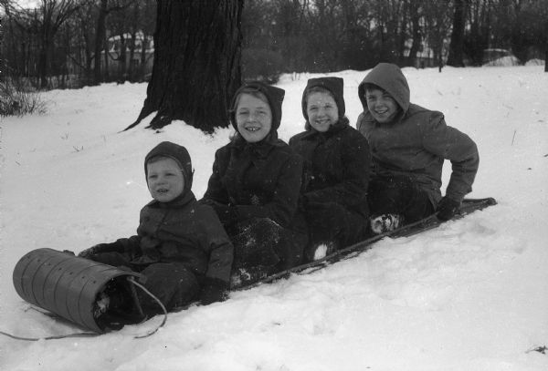Winter scene with the four children of Mr. and Mrs. Deane Adams, 843 Farwell Drive, Maple Bluff, on their toboggan. Left to right: Deane, Joan & Susan (twins) and Cameron.
