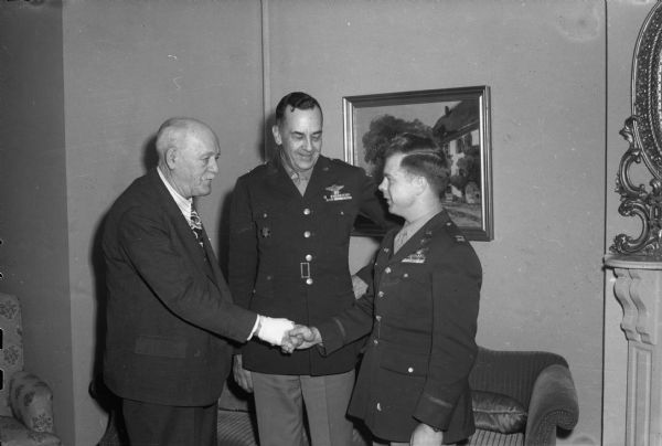 War hero Capt. Richard I. Bong, of Poplar, Wisconsin, credited with knocking out 21 Japanese planes in the South Pacific, shaking hands with Governor Walter Goodland at the Governor's Residence. Looking on is Brig. Gen. S.W. FitzGerald, commanding officer of Truax Field.