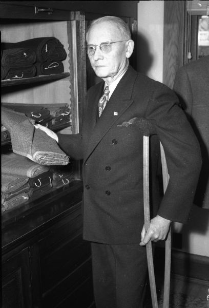 Portrait of John Simpson, who after an absence of several weeks caused by a broken hip suffered by a fall early in December, returned to Muller-Simpson Co. merchant tailoring firm.  While still using crutches, Simpson spent a few hours each day directing the cutting and fitting of clothes at the Muller-Simpson Co.