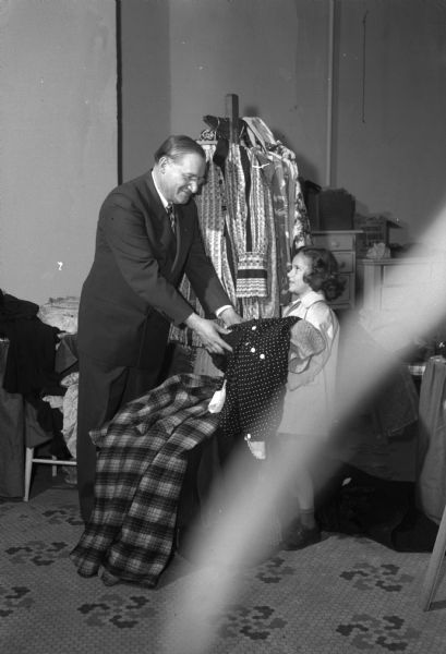 Joe Rothschild, Dane county chairman of the United National Clothing Collection, is shown receiving a donation from Barbara L'Hommedieu, daughter of Mr. and Mrs. C.H. L'Hommedieu, 1615 Summit Avenue. Mr. Rothschild stated that he was asked to be the chairman of the Clothing collection because "they were looking for the biggest sucker in town and — they wanted someone familiar with the old clothes business."