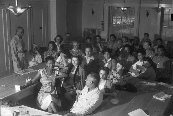 Students attending a lecture. The Abraham Lincoln School for Social Science, Chicago, Illinois, sponsored a Summer Institute in Madison for several summers, including 1945. The students who attended the two week sessions were mostly adult union workers and their families. They lived in rooming houses on Langdon Street and Lake Lawn Place, attended lectures and participated in recreational activities. The photographs show the teachers with groups of students, both indoors and out-of-doors, the students participating in recreational activities such as boating and badminton and the children with a day care worker. The School was run by former University of Wisconsin Associate Professor of Classics Alban D. Winspear. Their textbook was called "Why Work for Nothing" espousing Marx's theory of value.  The school had a communist / leftist philosophy and was often confused with the University of Wisconsin's School for Workers.