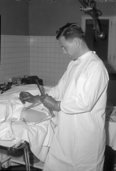 Capt. (Dr.) Gunnar Quisling is shown with a device (a surgical caliper or sliding square) he perfected for rapid detection of foreign bodies in wounded soldiers. Home on leave, he serves in England.