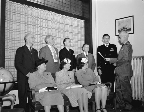 Lieut. Theordore Haspell is shown receiving four gold stars from Capt. J.E. Hurff, University of Wisconsin professor of naval science and tactics. The stars were awarded for meritorious acts during 15 flights in a navy patrol bomber over Japanese-held territory in 1945. Seated from left: Mrs. Ted Wilson, Mrs. Walter Haspell, and Mrs. H.L. Collier. Standing from left: C.F. Cramer, Ted Wilson, H.C. Kypke, unidentified man, Lieut. Haspell, and Capt. Hurff.