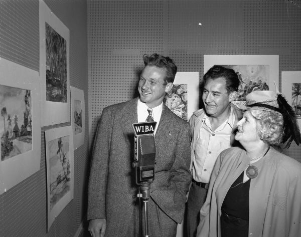 Robert Overman Hodgell (left), is shown viewing some of his paintings which were done while he was serving with the navy in the South Pacific.  Byron C. Jorns, Madison artist (center), and Mrs. Walter S. (Madge) Goodland are admiring Hodgell's work which went on display in the  WIBA Radio Broadcasting Studio, Room 414 Tenney Building, 110 East Main Street.