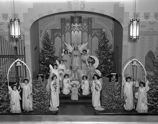 A scene from the Christmas Pageant presented at the Zion Lutheran Church, 247 Division Street. Angels are left to right: Arlene Jenkins, Mary Sachtjen, Elsa Splett, Shirley Schumann, Joanne Groff, Joan Scheiwe, Dorothy Schultz, and Mitzi Schlicht. Mary is portrayed by Alberta Smith. At the manger are Rochelle Dommershausen, Shirle Ann Becker, and Carole Schrotz. Also shown are four other unnamed angels.