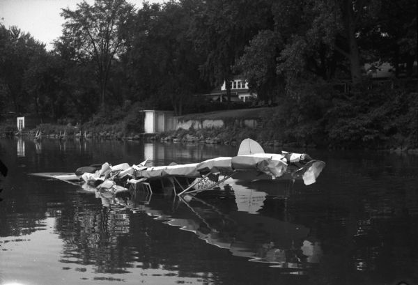 Rescue of airplane which has crashed into Lake Mendota near the north shore.  View of the airplane from the water toward the shore and Camp Wakanda. Tom Langlois, 17, 213 North Randall Avenue, was seriously injured when the routine solo training flight crashed into the lake.  He was rescued by an unidentifed fisherman.