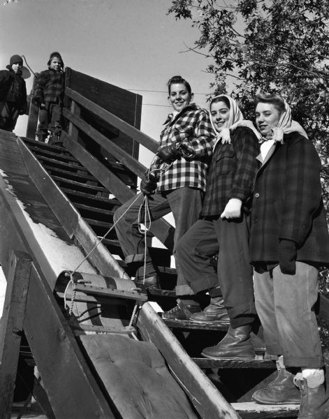 Three teenagers posing on the steps of the toboggan slide at Hoyt Park. Ascending the steps are Al Gay, Mary Homann, and Ruth Ann Gay. Two young boys are standing at the top of the steps looking down.
