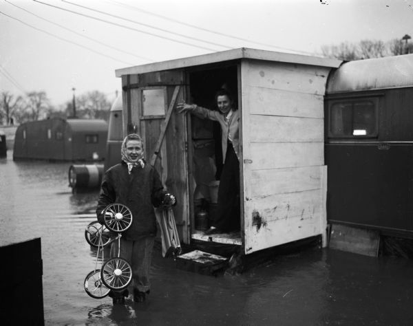 Flood at the University of Wisconsin-Madison East Hill Trailer Camp, located at 451 North Midvale Boulevard, south of University Avenue.  Shown are two of the students' wives who began moving belongings before the flood waters entered their small trailer homes. Mrs. Calvin Wilkes is holding a baby carriage and Mrs. Eugene Smith stands in a doorway.