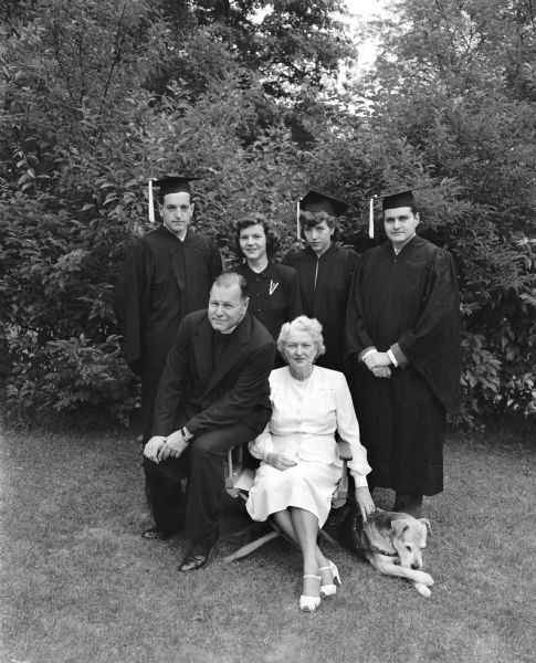 Group portrait of the Reverend and Mrs. Francis J. Bloodgood, former pastor of St. Andrews Episcopal Church, and their family, taken at their home, 1102 Lincoln Street. Seated in the foreground are Reverend and Mrs. Bloodgood. Standing left to right: Francis C. Bloodgood, twenty-four; Eve Bloodgood, seventeen; Jill Bloodgood, twenty, and Joseph W. Bloodgood, twenty-two. Francis, Jill and Joseph all earned their caps and gowns at the University of Wisconsin, where Eve is was student. The Reverend and Mrs. Bloodgood have also been attending classes at the university. A dog sits at Mrs. Bloodgood's feet.