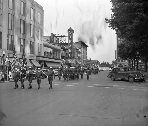State Eagles Convention Parade Kenosha Aerie Eagles Conventioneers marching in their 46th annual parade, on East Mifflin Street. Manchester's store, at the corner of Wisconsin Avenue and East Mifflin Street, and the Strand Theater, is shown in the background along with the Madison Hotel.