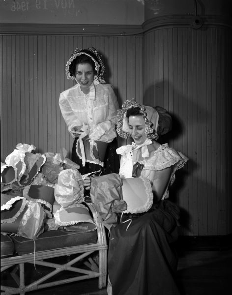 Members of the Madison Who's New Club at a barn dance in the YWCA gymnasium. Mrs. Edgar S. (Kathleen) Schreiber, left, chairman for the party, and Mrs. Robert Beverstein, 2928 Maher Avenue, check over the crepe paper bonnets, which were given as favors to women attending the barn dance.