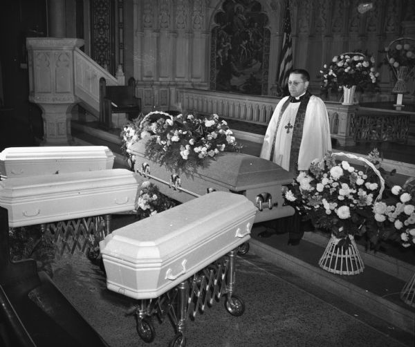 Dr. Charles A. Puls, pastor of Luther Memorial church, 1021 University Avenue, looks down on the caskets of a mother and her three children, during funeral services at the church. Florence Doreen Dinger and her children, Shirley, Billy and Judeen, died in a fire at their home on November 28, 1948.