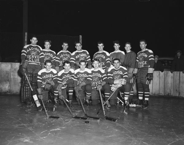 Group portrait of the Madison Cardinals ice hockey club (in uniform) sponsored by the Milwaukee Road Madison Service Club. The team was captained by Lee Fiscus and managed by John Riley, both of whom where players on the team.