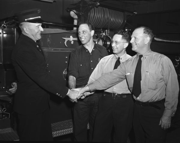 Assistant Fire Chief Sebastian C.A. Ratcliffe shaking hands with three fire fighters with whom he has teamed to fight many fires in Madison. The photograph was taken on the day of his retirement. The fire fighters, from left, are Fireman Edward Bokina, Lieut. Albert Rogg, and Capt. Erwin Beale.