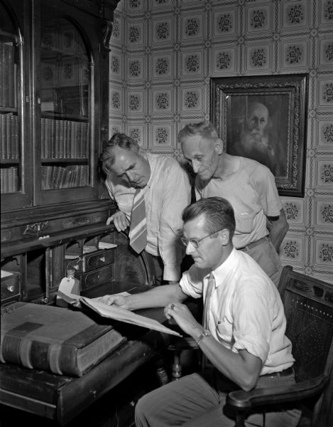 Looking over Governor Nelson Dewey's account books at the governor's desk in his office at Stonefield are Raymond Sivesind, state supervisor of historic sites, sitting; R.J. Eckstein, Cassville village president; and George W. Froehringer, caretaker of Nelson Dewey State Park.