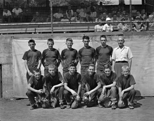 Mallatt Drugs Junior Boys Baseball Team Group portrait of the championship winning Mallatt Drugs junior boys baseball team. First row from left are: Jim Mahoney, Bob Walsh, Phil Green, Bill Mallatt, Tom O'Sheridan, and Fred Rogers. In the back row, left to right, are: Dan Hahn, Dan Jeffrey, Bob Clauson, Bill Marshall, Bill Mansfield, and sponsor Adolph Mallatt. People are sitting in the stands in the background.