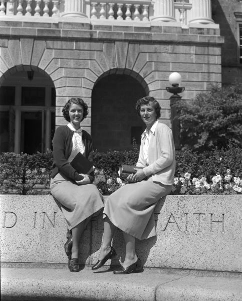 College Co-eds Joan Sexton and Mary Young Joan Sexton (left), daughter of Mr. and Mrs. Joseph (Eleanor) Sexton, 58 Cambridge Road, and Mary Young, daughter of Mr. E.J. (Alice) Young, Shorewood Hills are sitting on top of the circular wall and bench in front of Bascom Hall on the University of Wisconsin campus.