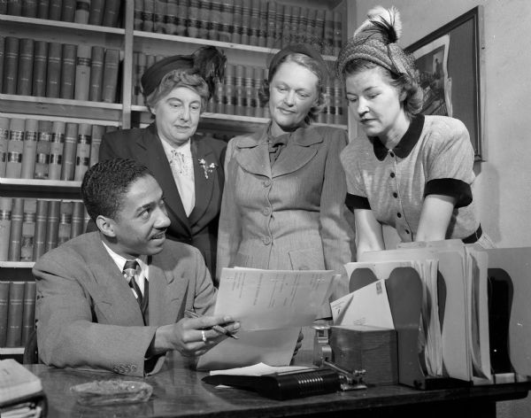 Charles Brown, student chairman of the Legal Aid Society, a Red Feather agency, describing the work of the society to three Community Chest women workers. From left are Esther Quast, Mrs. Jess (Melvina) Brown, and Mrs. Fred (Ann) Sayles.