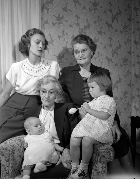 Four Generations of Family A reunion of four generations of the family of Minnie Miller, Long Beach, California, who is shown seated, holding her infant great-granddaughter, Terry Ann Reimann. Seated on the arm of the chair is the baby's sister, Jan Reimann. Standing are Mrs. Curtis (Doris) Reimann, 1149 Amherst Street, mother of the two girls, and Mrs. R.B. (Leila) Jerde, 2310 Van Hise Avenue, daughter of Mrs. Miller and mother of Mrs. Reimann.