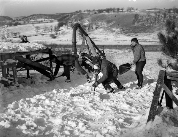 Members of the Blackhawk Ski Club prepare the landing area at the club's ski jump at Tomahawk Ridge, located west of Middleton. From left are Jim Jardine, Tommy Pharo, and Bob Higgins, shown shoveling snow into a conveyor which carries the snow into a silo filler for blowing it over the landing area.